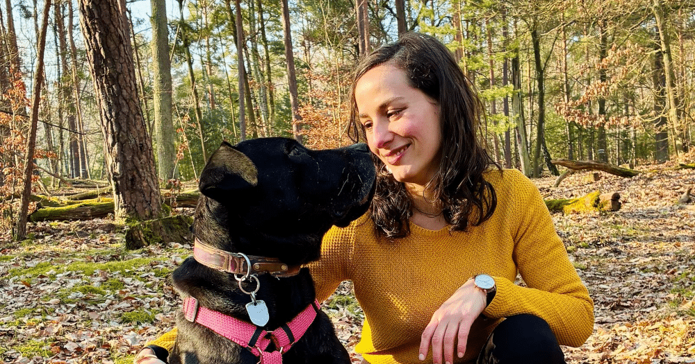 Femme accroupie à côté d'un chien noir dans la forêt