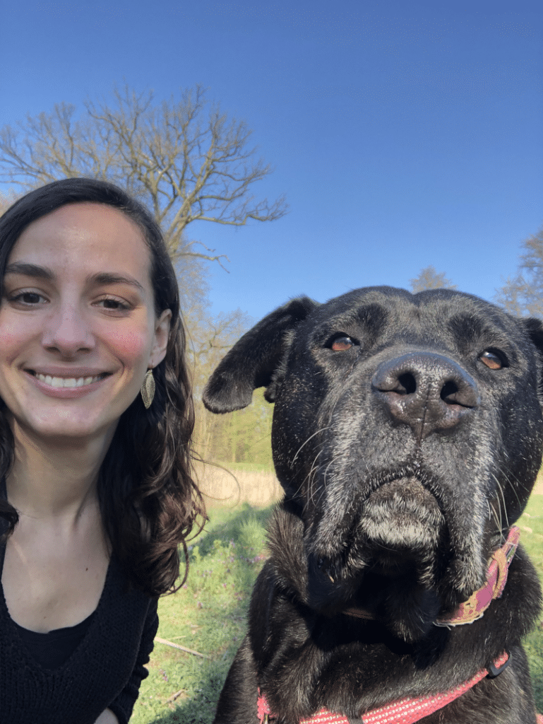 Femme assise dans une forêt à côté d'un grand chien noir