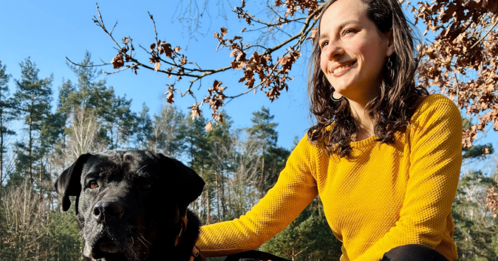 Femme assise dans une forêt à côté d'un grand chien noir