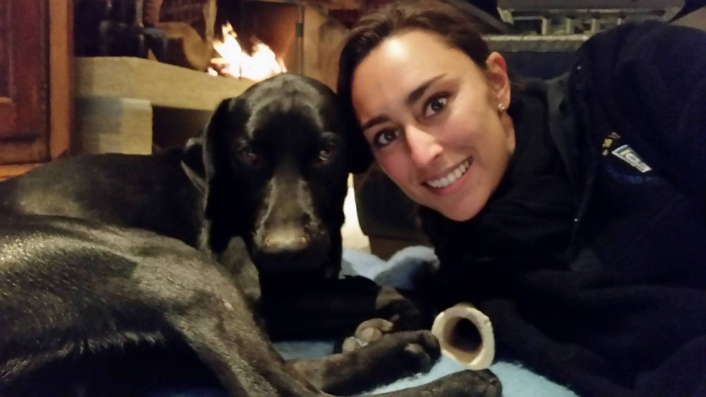 Jeune femme souriante allongée à côté d'un chien noir couché.