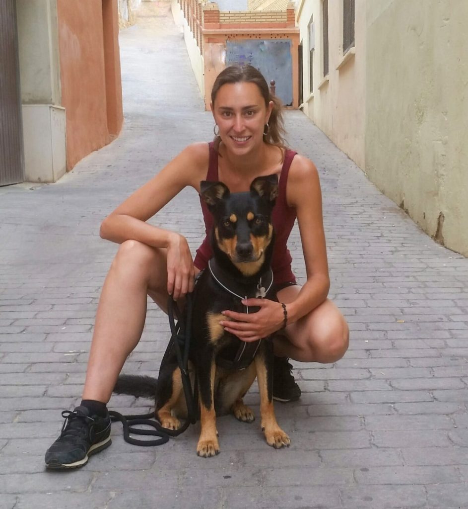 Jeune femme brune accroupie dans une rue avec un chien assis.
