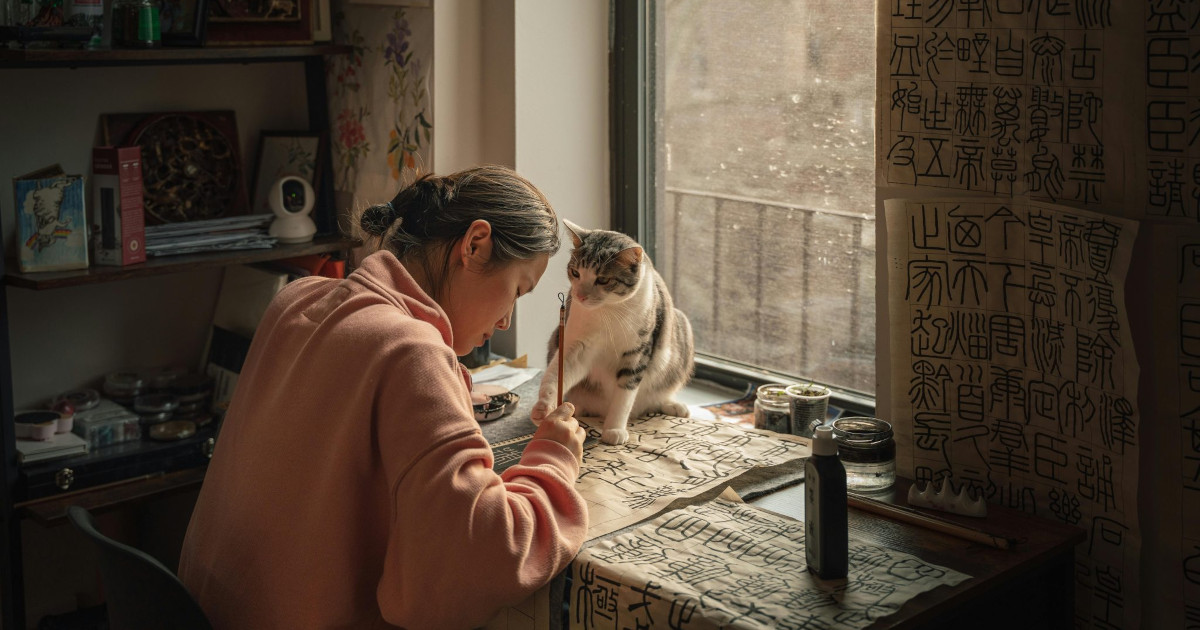 Femme pratiquant la calligraphie chinoise à côté d'un chat curieux dans une atmosphère calme