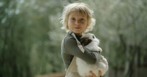 Blond child carrying a rabbit in a forest