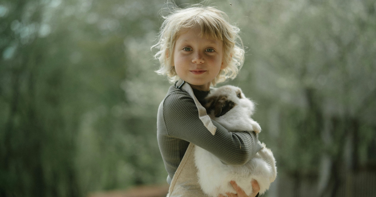 Blond child carrying a rabbit in a forest