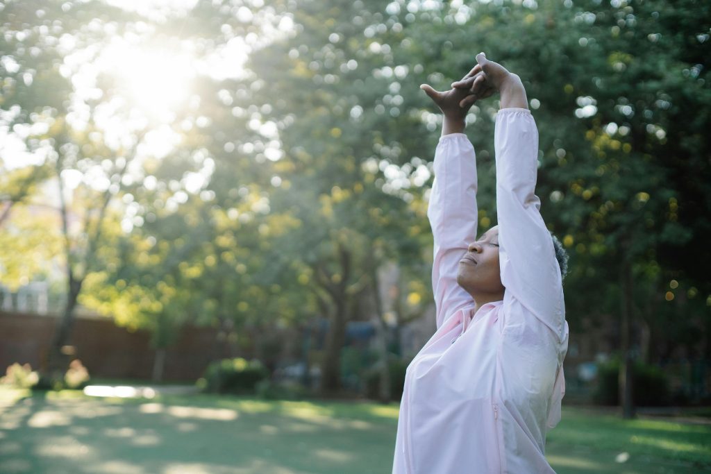 Woman enjoying a stretch in a peaceful, sunlit park setting outdoors.
